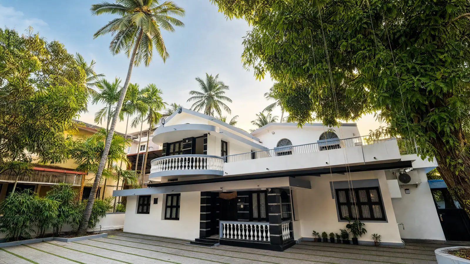 The white house rising under tall coconut palms and old trees at Spanda