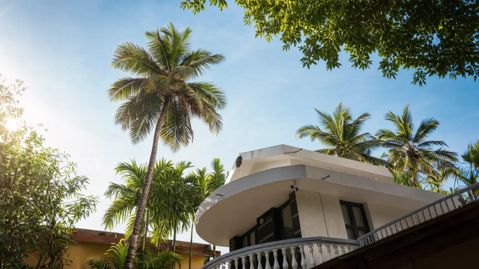 The signature curved balcony, framed by coconut palms against a clear Udupi sky.